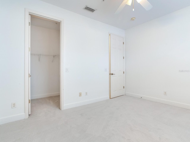 unfurnished bedroom with a closet, a walk in closet, light colored carpet, and ceiling fan