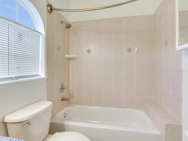 bathroom featuring tiled shower / bath combo, toilet, and a wealth of natural light