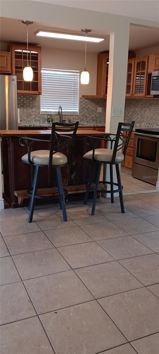 kitchen featuring hanging light fixtures, decorative backsplash, light tile patterned flooring, a kitchen bar, and stainless steel appliances