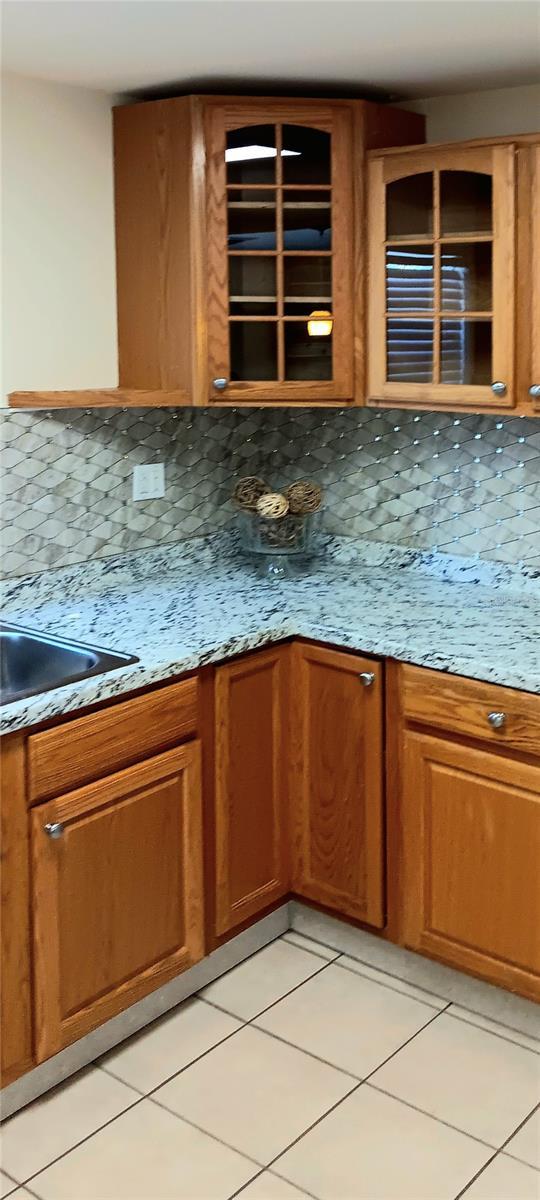 kitchen featuring light stone countertops, backsplash, sink, and light tile patterned flooring