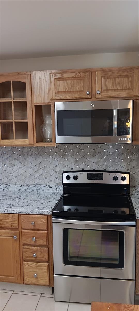 kitchen with light stone countertops, stainless steel appliances, light tile patterned floors, and tasteful backsplash