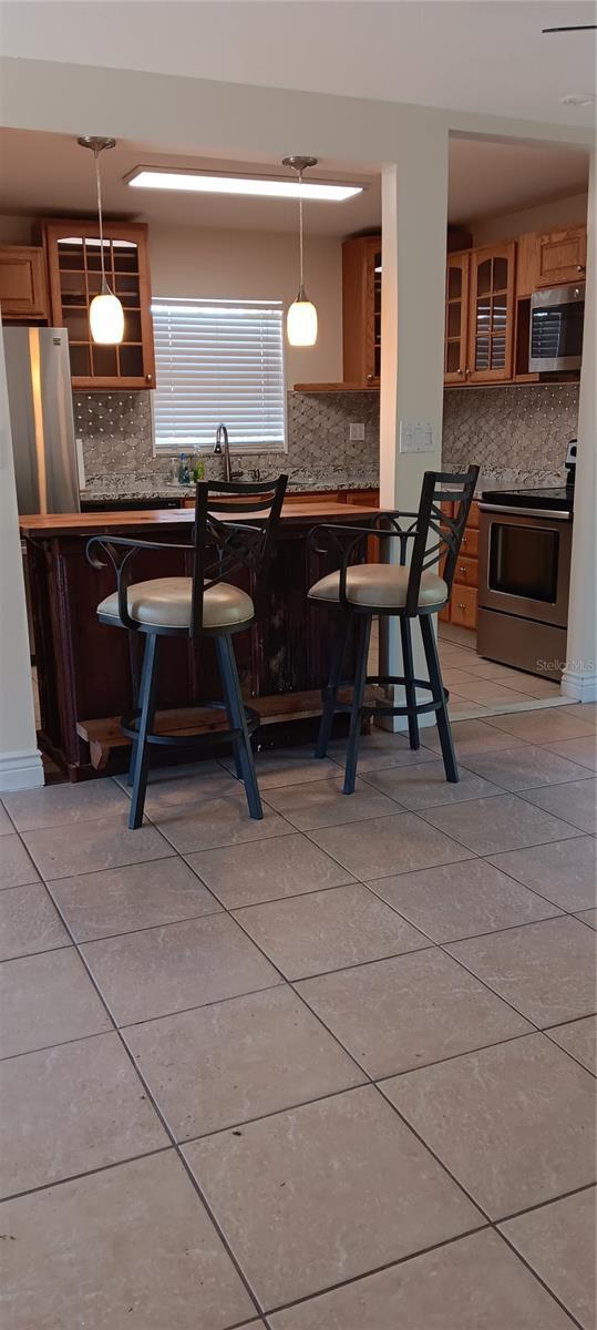 kitchen featuring backsplash, stainless steel appliances, hanging light fixtures, and a breakfast bar area