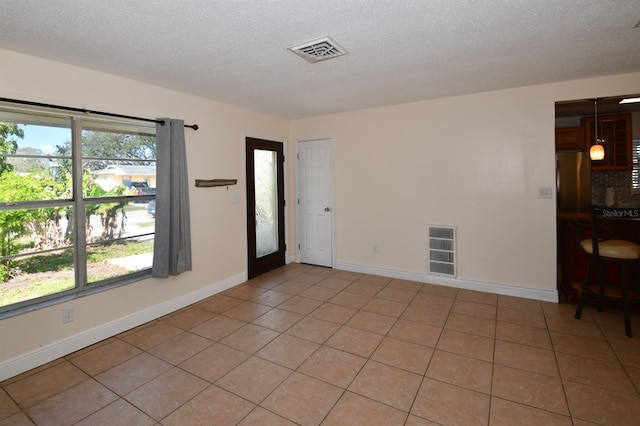 spare room with a textured ceiling, light tile patterned flooring, visible vents, and baseboards