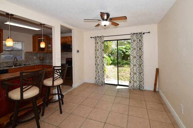 dining area featuring light tile patterned floors, ceiling fan, a textured ceiling, and baseboards