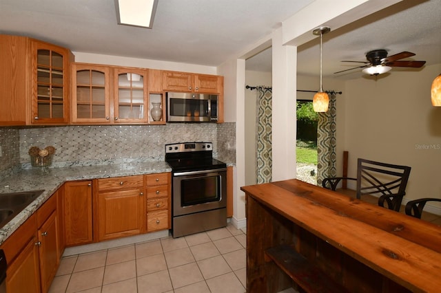 kitchen featuring appliances with stainless steel finishes, light tile patterned flooring, light stone countertops, and decorative backsplash