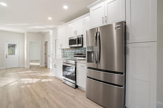 kitchen with white cabinets, backsplash, light wood-type flooring, and stainless steel appliances