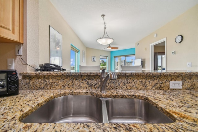 kitchen featuring stone counters, sink, and ceiling fan