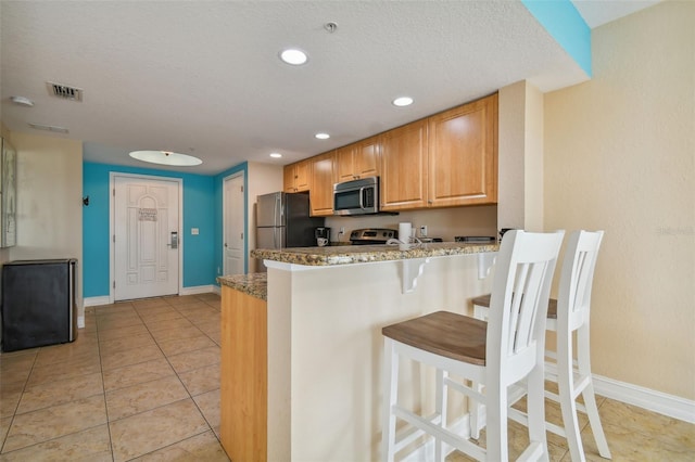 kitchen featuring stainless steel appliances, kitchen peninsula, a textured ceiling, a kitchen bar, and light tile patterned floors