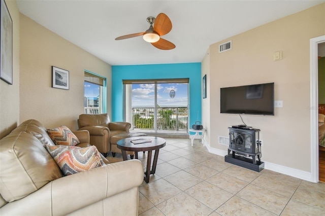 living room with ceiling fan, a wood stove, and light tile patterned floors