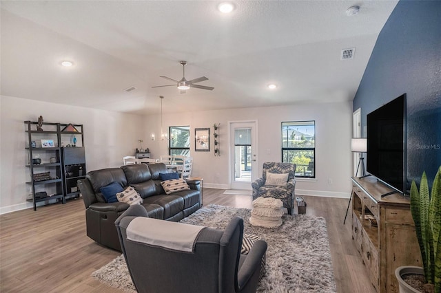 living room featuring ceiling fan with notable chandelier, light hardwood / wood-style floors, and vaulted ceiling