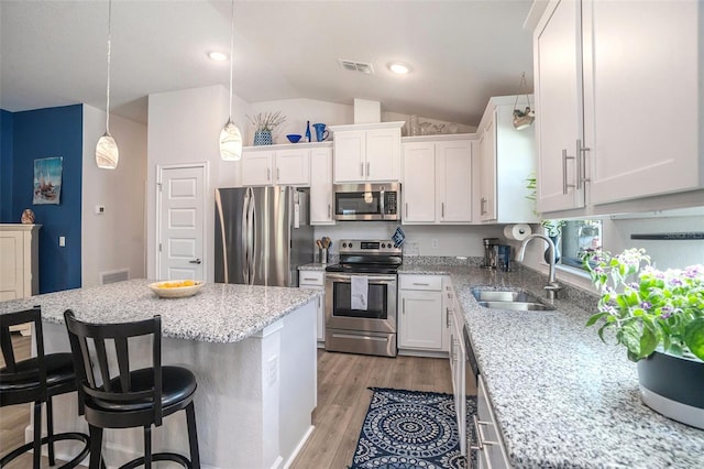 kitchen featuring lofted ceiling, hanging light fixtures, light wood-type flooring, appliances with stainless steel finishes, and white cabinetry