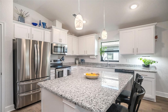 kitchen with appliances with stainless steel finishes, decorative light fixtures, a kitchen island, and white cabinets