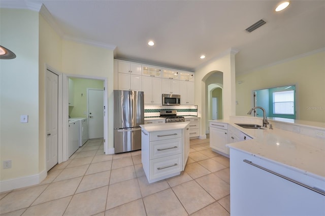 kitchen featuring white cabinets, sink, washing machine and dryer, ornamental molding, and stainless steel appliances