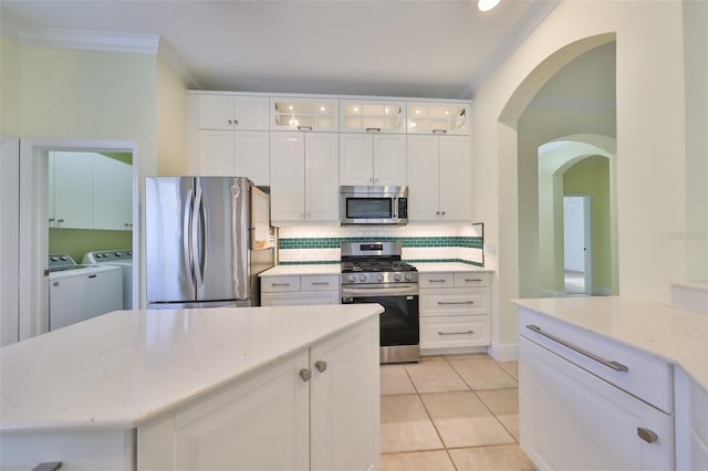 kitchen with ornamental molding, stainless steel appliances, washer and dryer, white cabinetry, and light tile patterned flooring