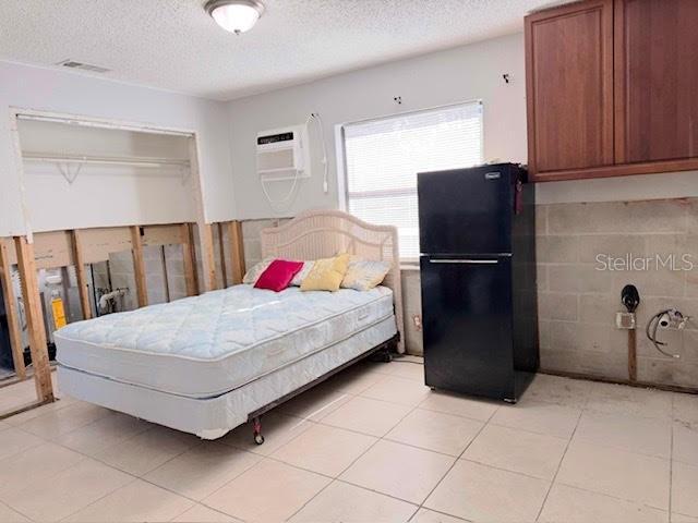 tiled bedroom featuring a textured ceiling, a closet, black fridge, and a wall mounted AC