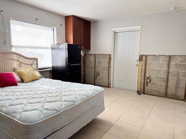 bedroom featuring light tile patterned floors, a textured ceiling, and black fridge