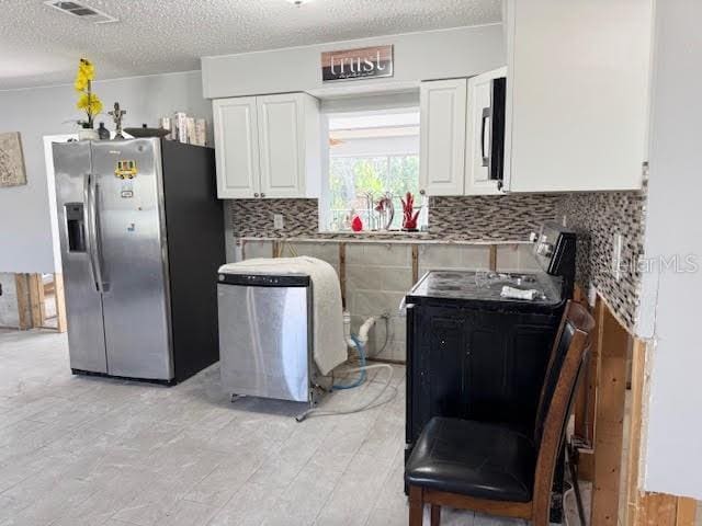 kitchen with white cabinets, a textured ceiling, stainless steel appliances, and tasteful backsplash