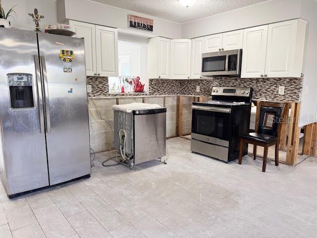 kitchen featuring decorative backsplash, white cabinetry, a textured ceiling, and appliances with stainless steel finishes