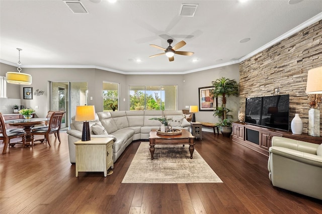 living room featuring dark hardwood / wood-style flooring, a stone fireplace, ceiling fan, and crown molding