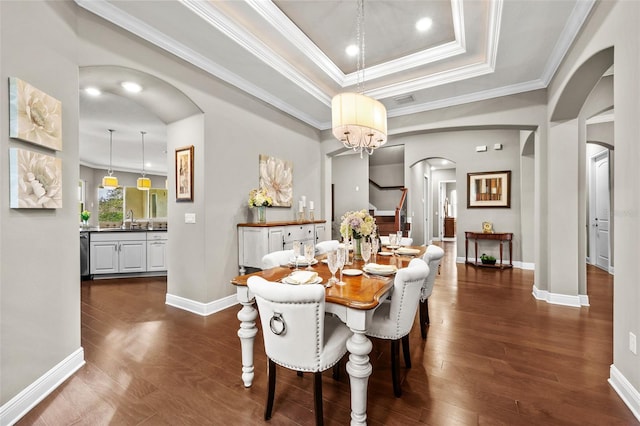 dining room featuring dark wood-type flooring, an inviting chandelier, crown molding, sink, and a tray ceiling