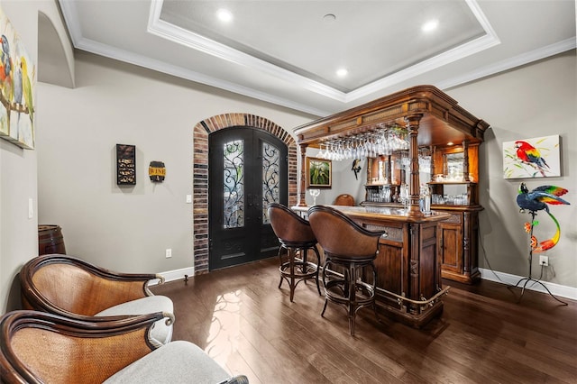 bar with a tray ceiling, dark wood-type flooring, and ornamental molding