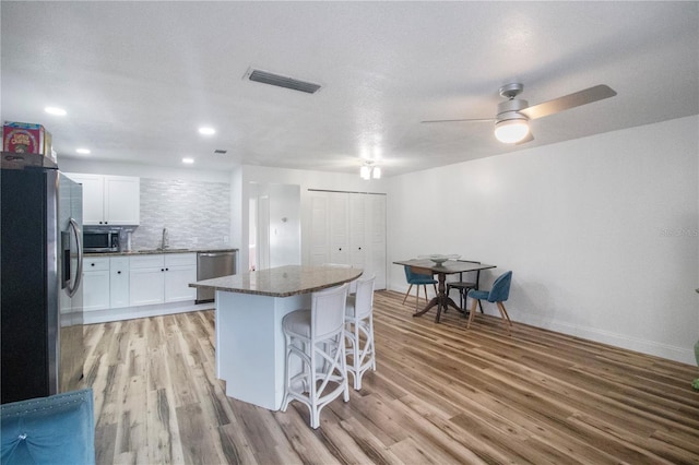 kitchen featuring white cabinets, appliances with stainless steel finishes, light hardwood / wood-style flooring, and a kitchen breakfast bar