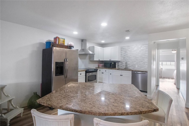 kitchen with a kitchen bar, appliances with stainless steel finishes, light wood-type flooring, wall chimney range hood, and white cabinetry