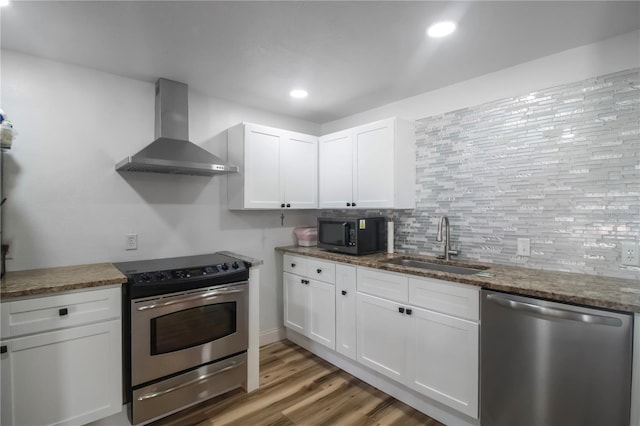 kitchen featuring stainless steel appliances, white cabinetry, hardwood / wood-style flooring, and wall chimney range hood