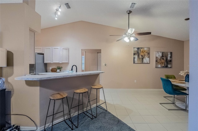 kitchen with kitchen peninsula, stainless steel fridge, a kitchen breakfast bar, white cabinetry, and lofted ceiling