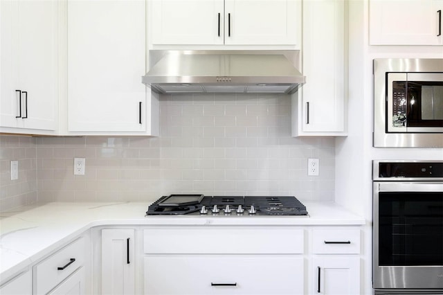 kitchen featuring backsplash, white cabinets, wall chimney range hood, and stainless steel appliances