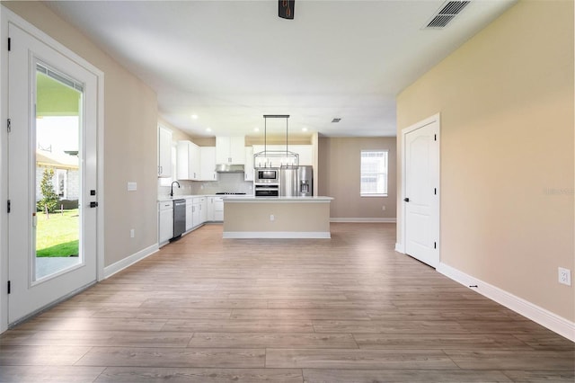 kitchen featuring white cabinets, hanging light fixtures, light hardwood / wood-style flooring, appliances with stainless steel finishes, and a kitchen island