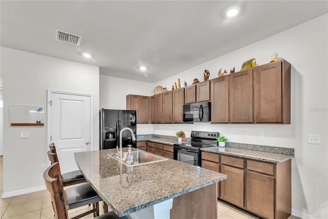 kitchen featuring black appliances, a center island with sink, sink, light tile patterned floors, and a breakfast bar area