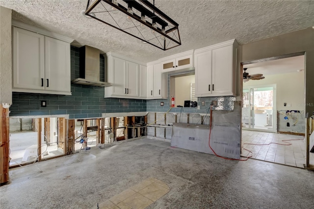 kitchen featuring white cabinets, decorative backsplash, ceiling fan, a textured ceiling, and wall chimney exhaust hood