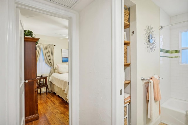 bathroom featuring ceiling fan, wood-type flooring, and tiled shower / bath