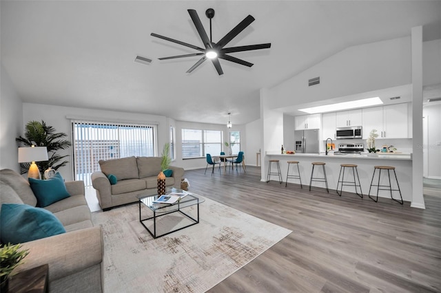 living room with ceiling fan, light hardwood / wood-style flooring, lofted ceiling, and sink