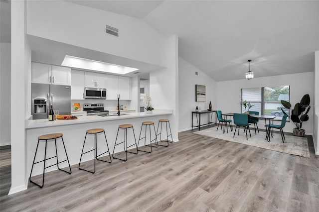 kitchen featuring white cabinets, kitchen peninsula, appliances with stainless steel finishes, and vaulted ceiling