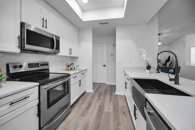 kitchen with light stone countertops, appliances with stainless steel finishes, sink, light hardwood / wood-style flooring, and white cabinetry