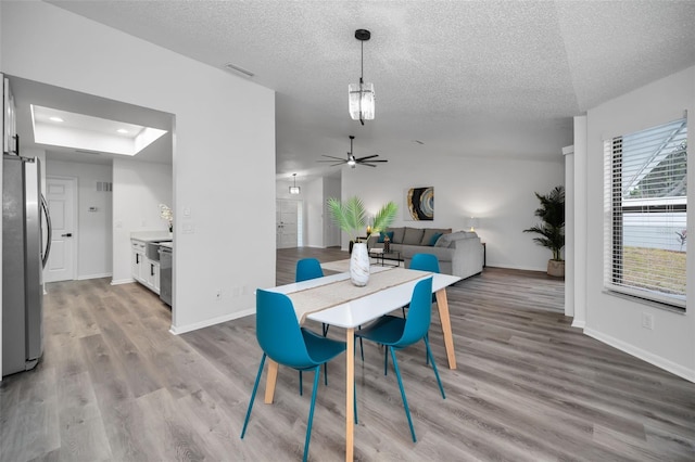 dining area featuring a textured ceiling, light hardwood / wood-style flooring, ceiling fan, and vaulted ceiling