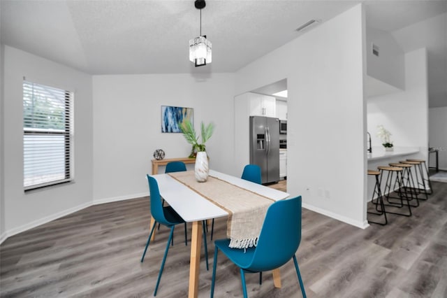 dining room featuring lofted ceiling, dark wood-type flooring, and a textured ceiling