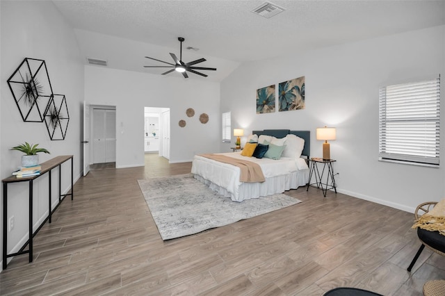 bedroom with lofted ceiling, ceiling fan, light wood-type flooring, a textured ceiling, and a closet