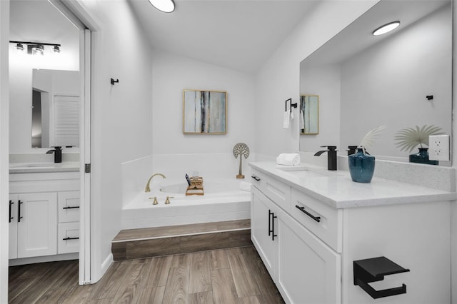 bathroom featuring wood-type flooring, vanity, a relaxing tiled tub, and lofted ceiling