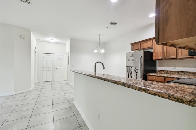 kitchen with a notable chandelier, light tile patterned flooring, dark stone counters, hanging light fixtures, and stainless steel refrigerator