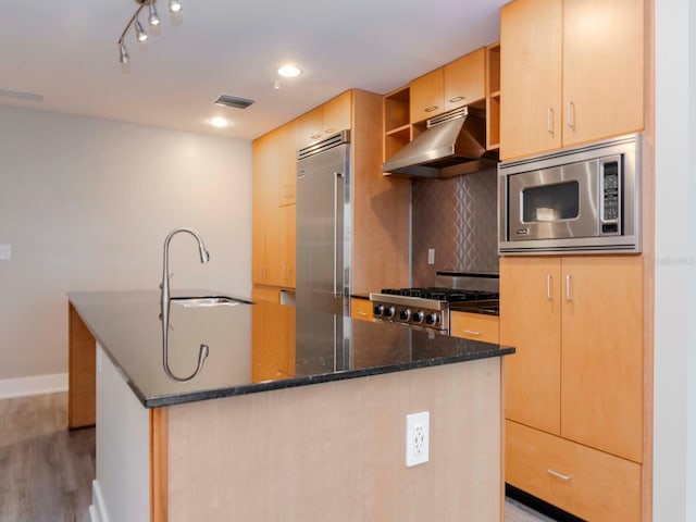 kitchen with light brown cabinetry, light wood-type flooring, sink, built in appliances, and dark stone countertops