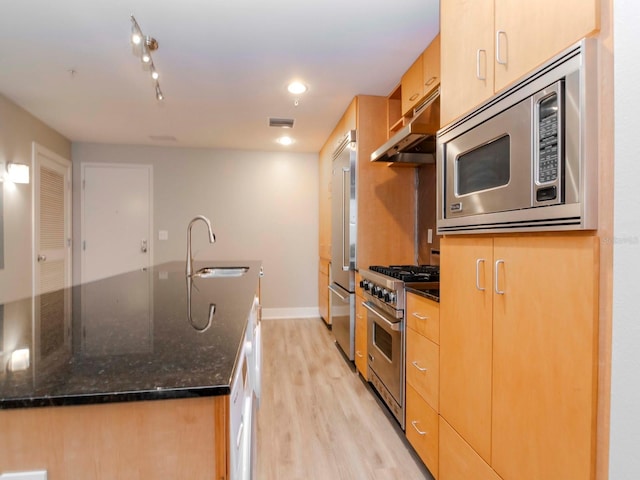 kitchen featuring sink, high quality appliances, dark stone counters, a kitchen island with sink, and light wood-type flooring