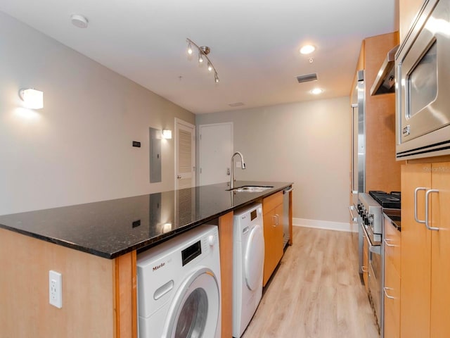 kitchen featuring appliances with stainless steel finishes, sink, dark stone countertops, light hardwood / wood-style floors, and an island with sink