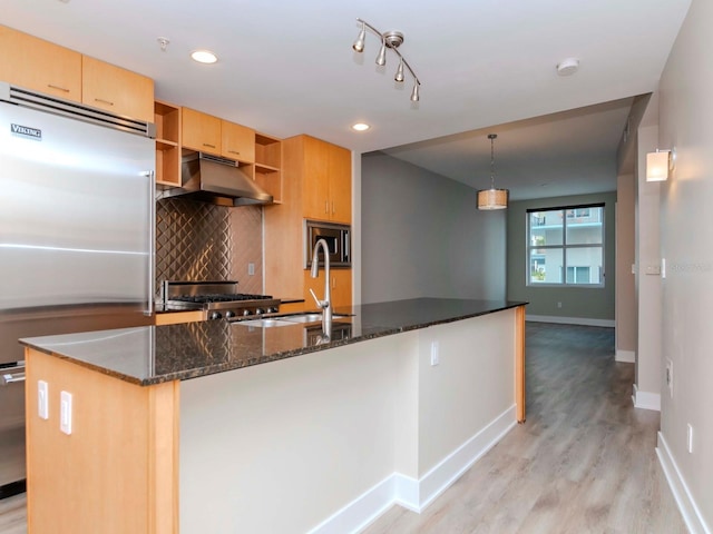 kitchen with hanging light fixtures, tasteful backsplash, light hardwood / wood-style flooring, built in appliances, and dark stone counters