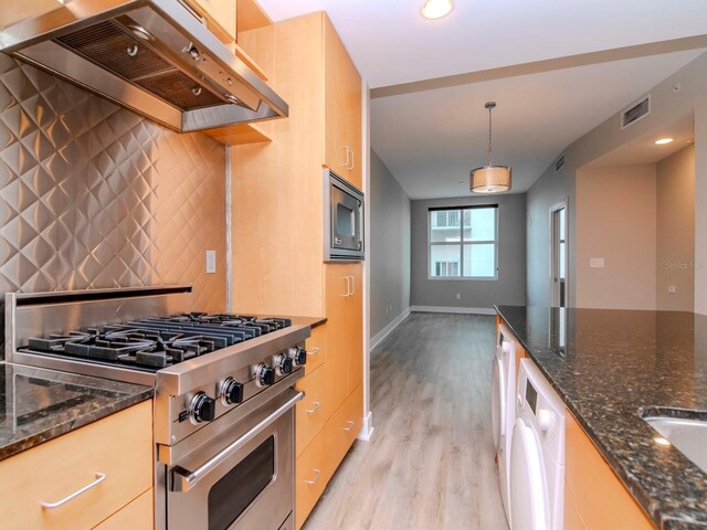 kitchen with stainless steel appliances, light hardwood / wood-style flooring, dark stone countertops, hanging light fixtures, and range hood