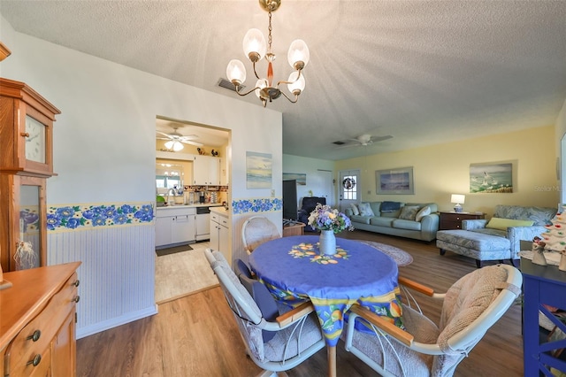 dining space featuring sink, ceiling fan with notable chandelier, light hardwood / wood-style floors, and a textured ceiling