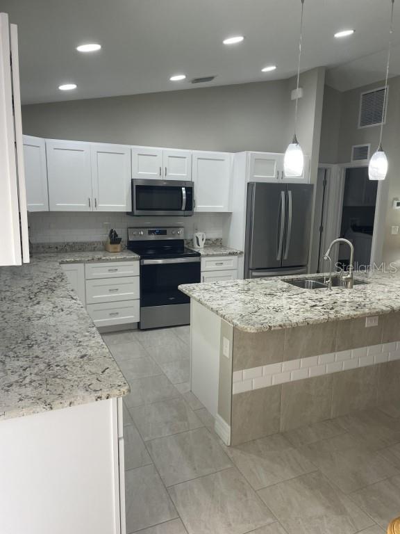 kitchen featuring appliances with stainless steel finishes, vaulted ceiling, sink, decorative light fixtures, and white cabinets