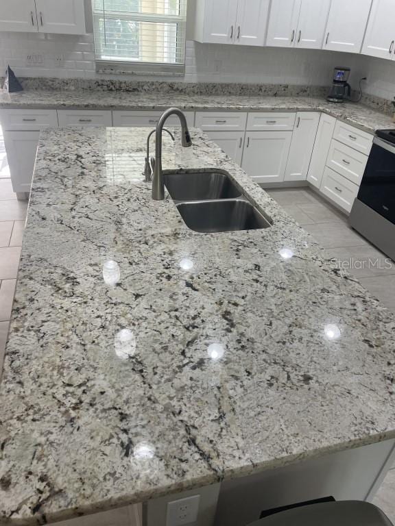 kitchen with electric range, white cabinetry, light stone countertops, and sink